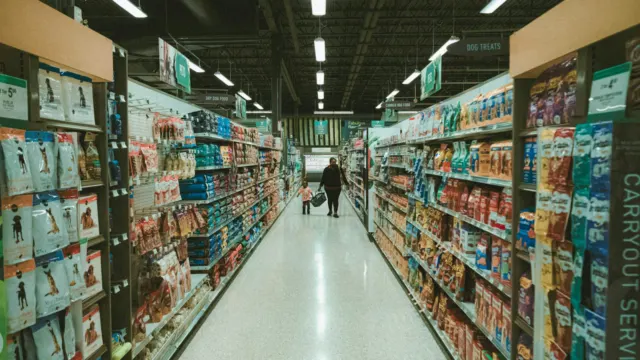 Shopper walking down a brightly lit supermarket aisle lined with packaged goods
