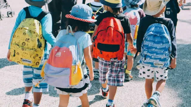 Young children with colourful backpacks and hats walking together on a path