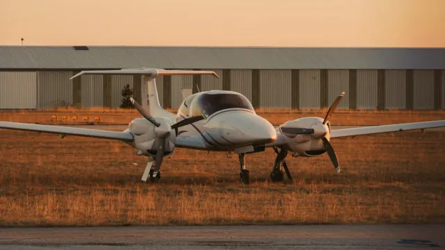 Small twin-engine propeller plane parked on an airfield in warm evening light