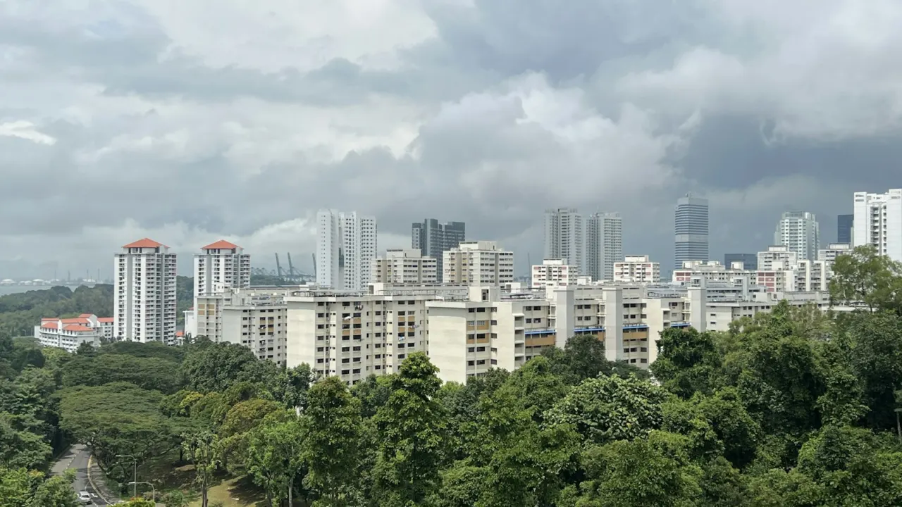 Mid-rise and high-rise residential blocks rising above a band of green trees under a cloudy sky