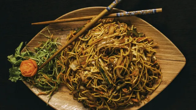 Stir-fried noodles with vegetables on a wooden platter with chopsticks