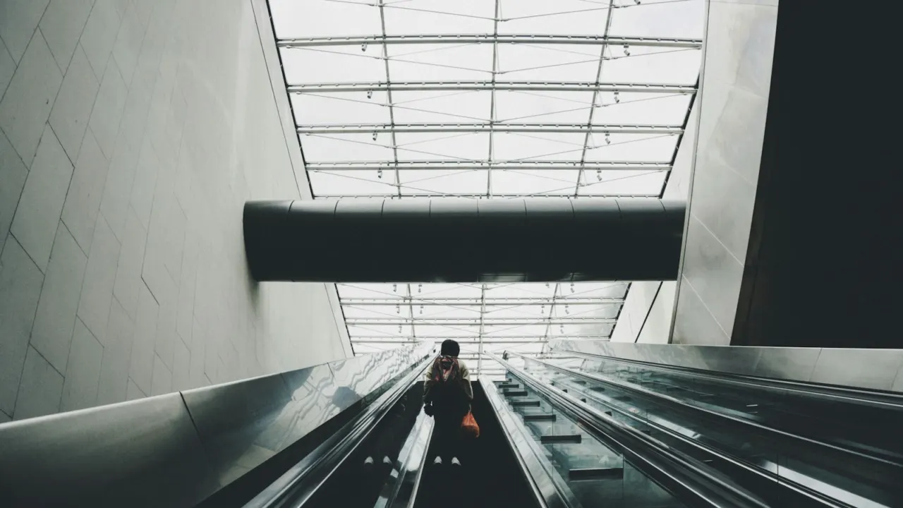 Commuter riding a long escalator towards a skylit station exit