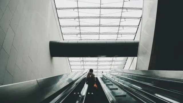 Commuter riding a long escalator towards a skylit station exit