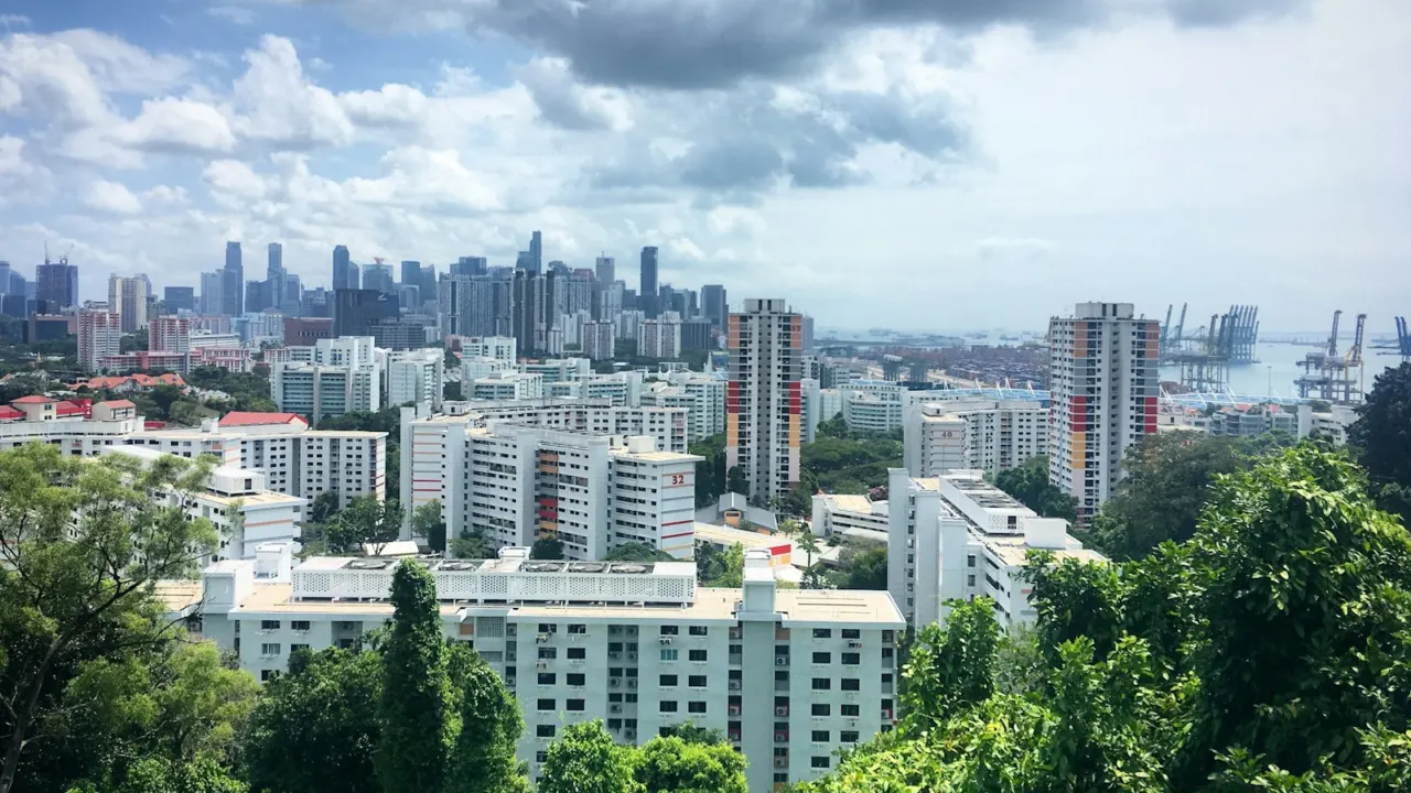 Residential blocks among thick green trees with city towers on the horizon under a cloudy sky