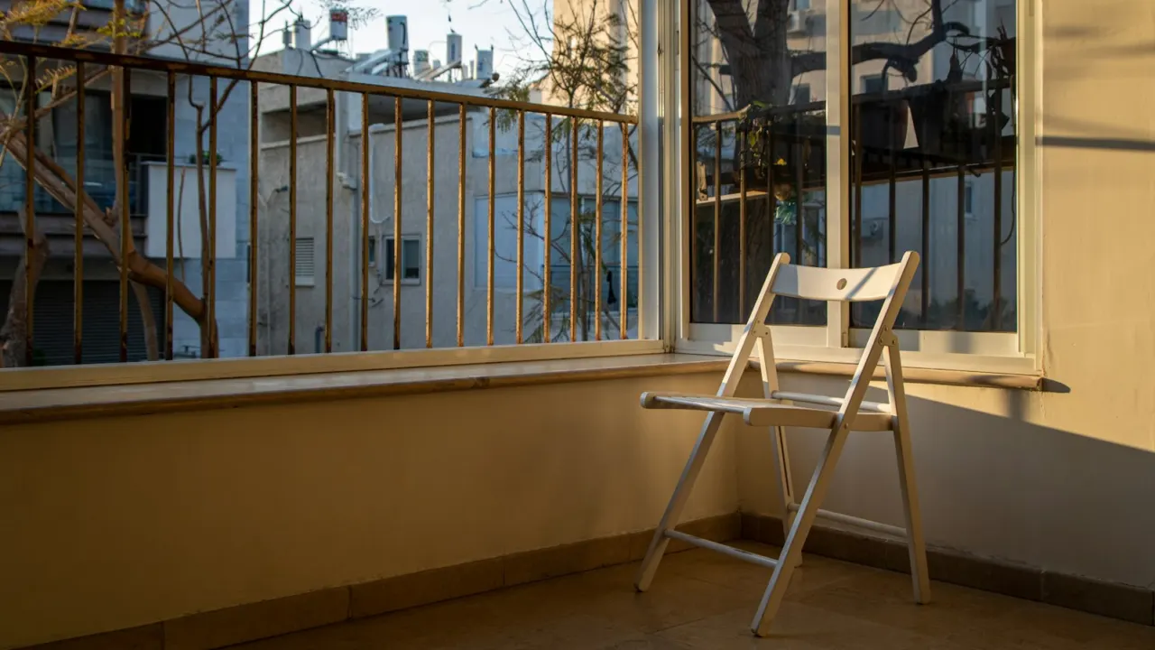 White folding chair beside an open balcony door in a sunlit apartment