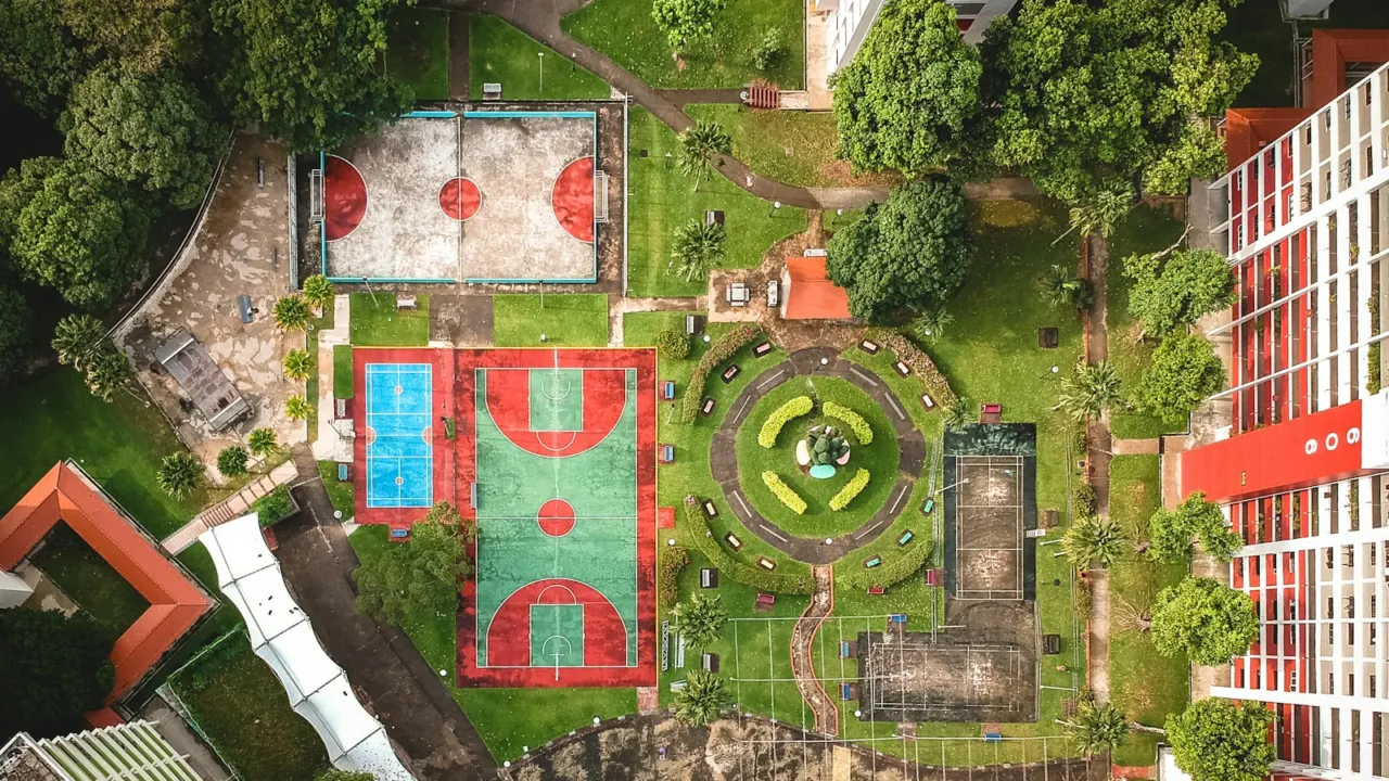 Aerial view of two outdoor basketball courts among trees beside tall apartment blocks