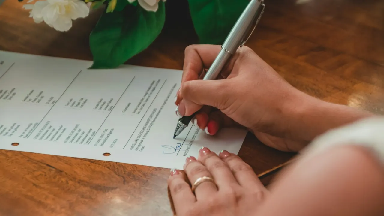 Person signing a printed agreement with a silver pen on a wooden table