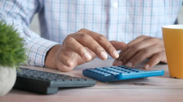 Person working out figures on a calculator at a desk next to a coffee mug