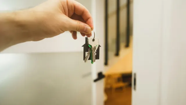 A hand holding up a door key beside a white front door
