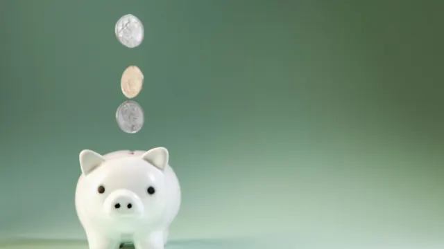 Coins dropping into a white piggy bank