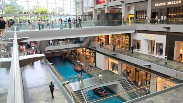 Shoppers walking across the open atrium levels of a large multi-storey Singapore mall