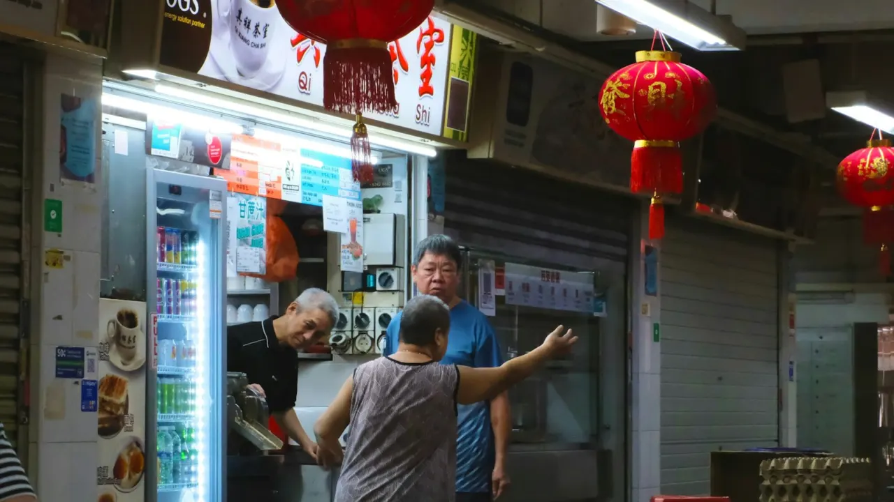 Stall owner serving customers at a brightly lit coffee shop hung with red lanterns